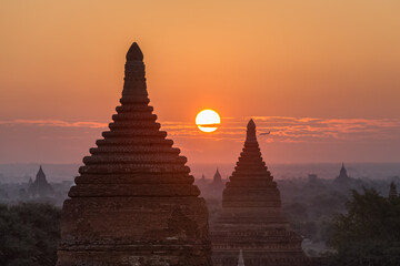 Sunrise over ancient pagodas in Bagan (Pagan), Myanmar, with a silhouette of descending plane on horizon. Bagan is an ancient city with thousands of buddhist temples and stupas