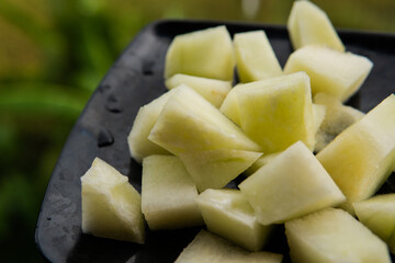chopped pieces of melon on a black plate in the hands of a girl
