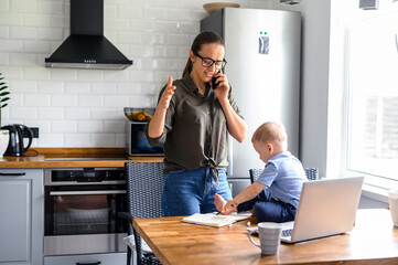 Business mom working at home. Woman talks on the phone while kid is painting in her working papers