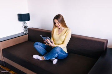 Obraz premium Happy young woman enjoying an e-book on her tablet computer as s
