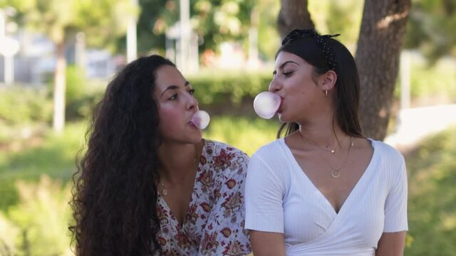 Multi-ethnic women chewing gum and blowing pink bubbles outdoors