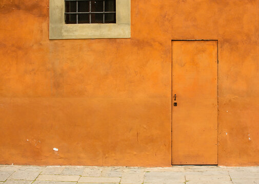 Orange plastered wall with door and window in it. Bright colorful photo wallpaper or background with space for text on the left.