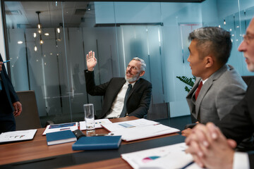 I have an idea. Happy mature businessman in formal wear raising his hand while having a meeting in the modern office