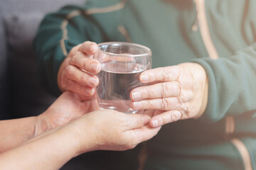 Grandmother with a glass of water, granddaughter gives grandmother a glass of water