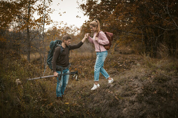 Hiking in nature. Young Man and Woman backpackers descend from the slope holding hands and holding...