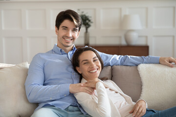 Portrait of smiling young man and woman sit relax n sofa at home hugging and cuddling, happy...
