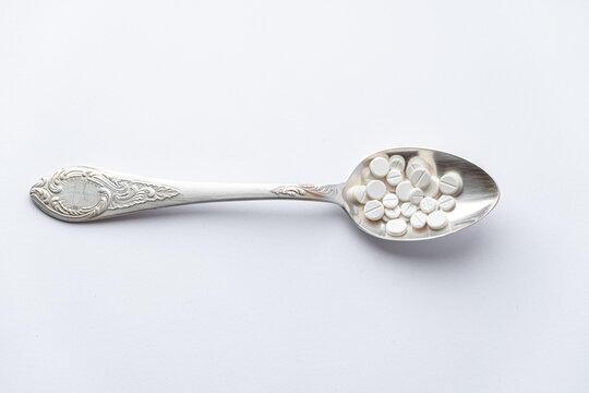 Medicine and health, treatment, pharmacy, coronavirus, pandemic, epidemic concept - layout one silver big tablespoon with different pills and capsules on a white background copy space.