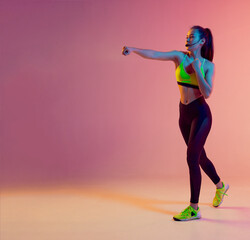 Cute girl fitness instructor teaches Boxing or body combat online training remotely on a bright neon background.