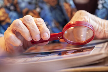 An old grandmother examines a book at the table with a magnifying glass.