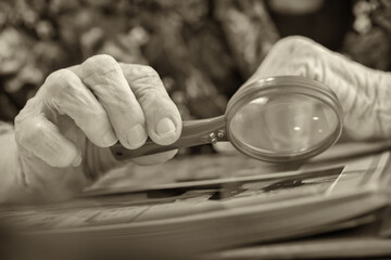 Fototapeta na wymiar An old grandmother examines a book at the table with a magnifying glass.