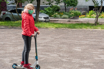 little blonde, pretty girl sitting on the playground, in a medical mask, with a scooter, during quarantine, due to a pandemic, isolation 