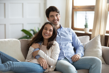 Obraz premium Portrait of happy loving young caucasian couple relax on couch in living room hugging and cuddling, smiling millennial man and woman rest on sofa embracing, enjoy romantic weekend at home together