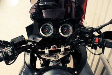 The arrow speedometer of a motorcycle on the steering wheel that stands on a concrete road closeup. Colored dashboard with sport bike handles, top view. Horizontal image of a tachometer gauge.