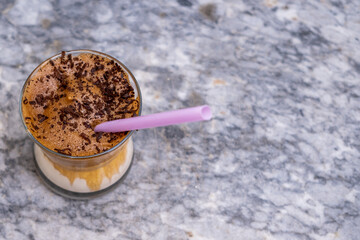 Top view of iced dalgona coffee with chocolate chips and pink straw on marble background,Korean iced coffee. Copy space for text