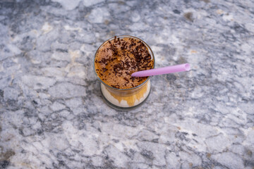 Top view of iced dalgona coffee with chocolate chips and pink straw on marble background,Korean iced coffee. Copy space for text