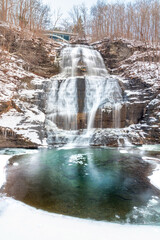 Multi tiered waterfall cascading down rocks in a snowy winter wonderland scene. She-Qua-Ga Falls -...