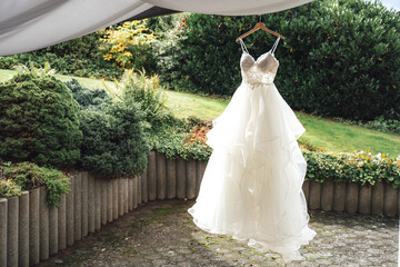 Bride's wedding gown on hanger on fresh air. Green outdoor park background. Wedding day concept.