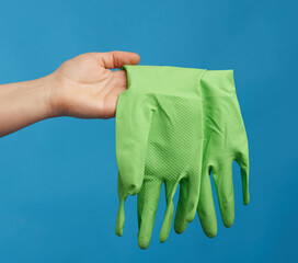 female hand holds green rubber gloves for cleaning, blue background