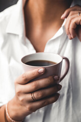 Woman in a white t-shirt holds morning coffee in a pink ceramic cup. Manicure. Front view