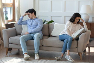 Unhappy young caucasian couple sit on sofa at home back to back think of breakup or divorce, upset millennial man and woman have family fight disagreement, struggle with relationships problems