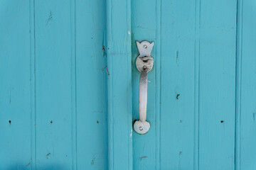 Turquoise wooden door with silver handle. Exterior design, traditional Mediterranean style. Close up.