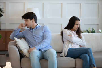 Mad offended man and woman sit separately back to back on couch at home having family fight or quarrel, unhappy young couple ignore avoid talking after disagreement, breakup, divorce concept