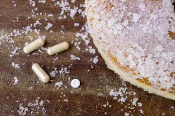 Close up top view of sweet sugar doughnut and medicine pills on wooden background. Concept of diabetes, obesity, unhealthy fast food 