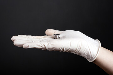 ear jewelry, hand in a white disposable glove holds in his palm a tunnel for the ear of silver color on a dark background close-up