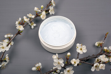 Obraz na płótnie Canvas white round body scrub with branches of white flowers of cherry on a gray background close-up, cleansing cosmetics skin care