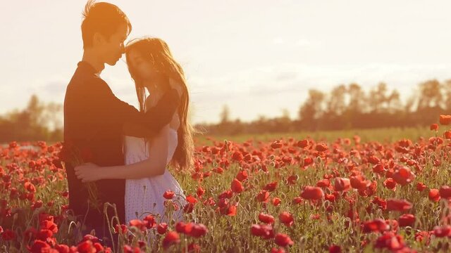 an Asian guy and a European girl hug and kiss on the border of a poppy and wheat field at sunset