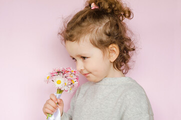 Obraz na płótnie Canvas little beautiful girl sniffs bouquet of daisies on pink background. happy birthday, mother's day