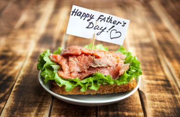 Red fish sandwich on rye bread with lettuce leaf on a dark wooden background. A note of congratulations.
