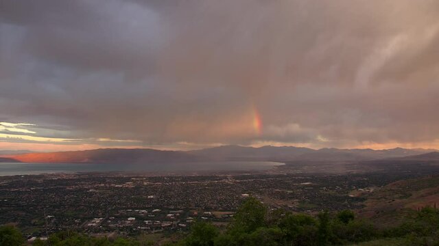 Panning view over Utah Valley as storm rolls through at sunrise and rainbow forms over the city of Orem.