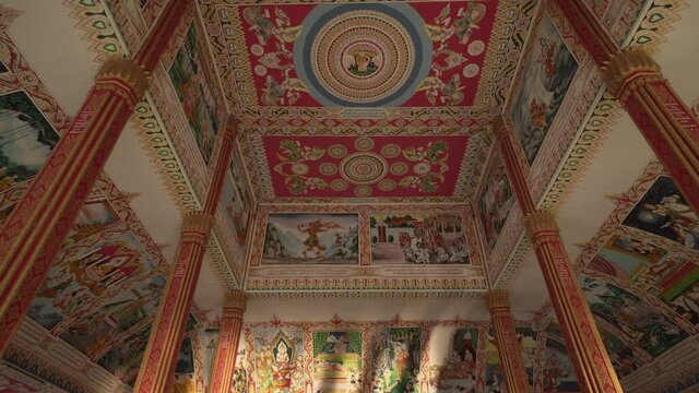 Tilt Up shot of paintings on ceiling with carvings over columns at famous Buddhist temple - Vientiane, Laos