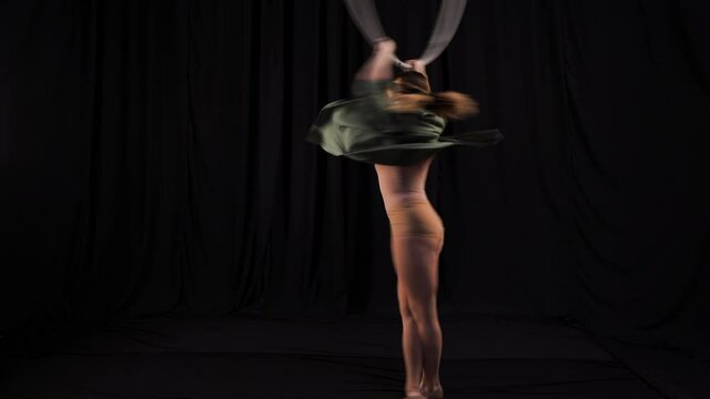 Sports girl circus actress fast rotates, spinning on aerial hoop on an even background. black backstage in the theater. European aerialist performer