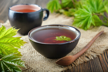 Bowl of maple syrup, tea cup and fresh green maple leaves on wooden table.