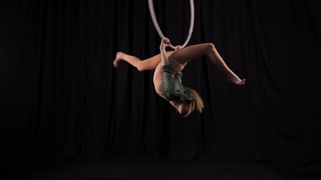 Girl circus gymnast performs a show on the air hoop. flexible acrobat spins on a ring in the air on a black background. slender young girl performs split in the air