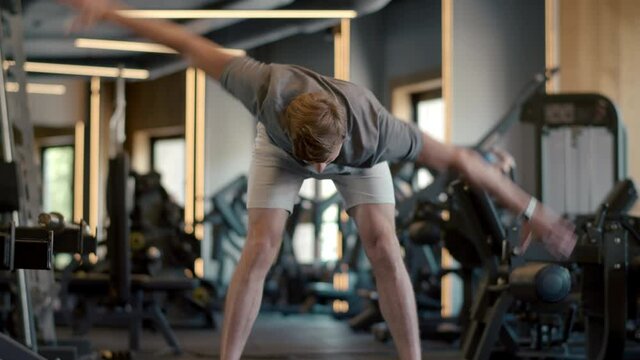 Handsome strongman making hand swings at gym. Sportsman warming up in sport club