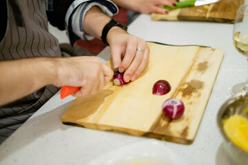 Man cuts onions close-up. People making salad together awaiting guests. Concept of home cooking healthy food.