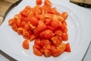 Chopped tomato on a white plate. People making salad together awaiting guests. Concept of home cooking healthy food.