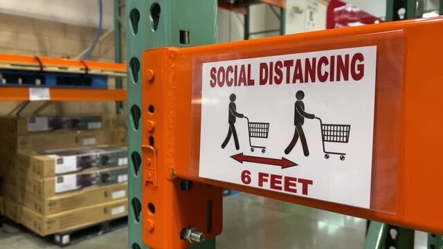 A shopper walks past a social distance reminder sign in a large big box store warehouse. Physical distancing was a common practice to reduce the spread of COVID-19 during the pandemic of 2020.	