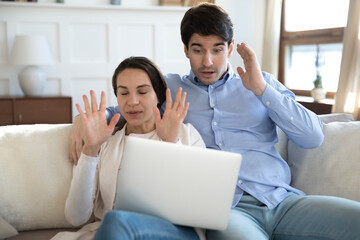 Young caucasian couple relax on sofa at home frustrated by internet video content or spam on laptop, confused millennial man and woman disappointed by computer operational problem or virus attack