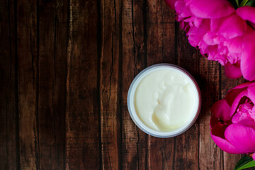 Natural anti-ageing moisturizing face cream decorated with bright pink peony flowers on rustic wooden background