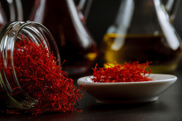 Dried saffron threads in a glass bottle and oil extract on a black background.