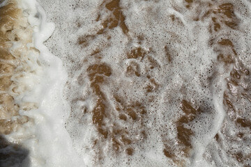 Sea water and the white foam on the beach in Golden sunshine, yellow sand