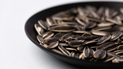 Black sunflower seeds in a dish on white background.