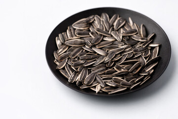 Black sunflower seeds in a dish on white background.