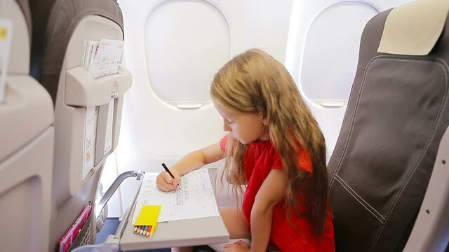 Adorable little girl traveling by an airplane. Kid drawing picture with colorful pencils sitting near aircraft window