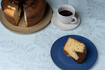 HOMEMADE RUSTIC CAKE, ON THE TABLE HAVING A CUP OF COFFEE IN THE BACKGROUND