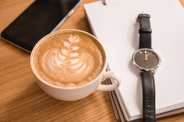 Cup of tasty coffee with notebook, clock and mobile phone on table in cafe
